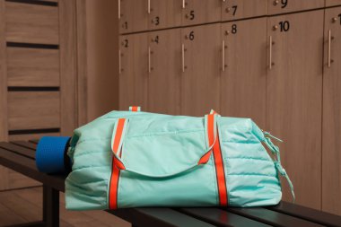 Spor çantası ve yoga minderi soyunma odasındaki ahşap bankta.
