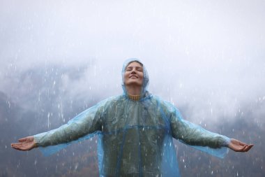Yağmurluklu genç kadın dağlarda yağmurlu havanın tadını çıkarıyor.