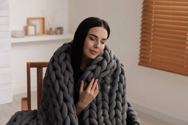 Evdeki koltukta örgü ören genç bir kadın.