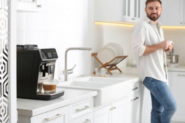 Genç adam mutfakta taze aromatik kahveyi seviyor, modern makineye odaklan.
