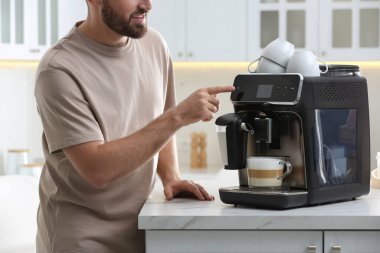 Genç adam mutfakta modern makineyle taze aromatik kahve hazırlıyor.