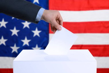 ABD 'de seçim. Adam oyunu sandığa ve arka planda Amerikan bayrağına koyuyor.