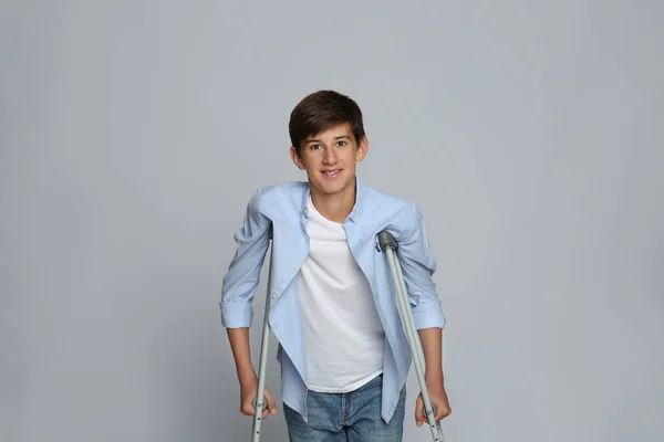 Teenage Boy Injured Leg Using Crutches Grey Background — Stock Photo, Image