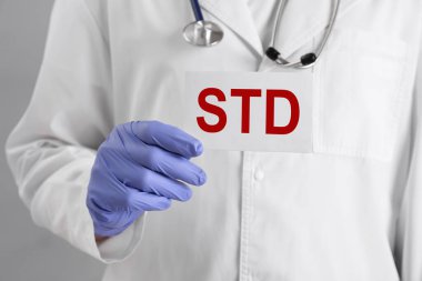 Gri arka planda STD kısaltması olan kağıt tutucu doktor, yakın plan.