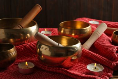Tibetan singing bowls with mallets and burning candles on red fabric clipart