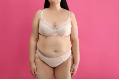 Pembe arka planda bej iç çamaşırlı şişman kadın, yakın plan. Büyük boy model