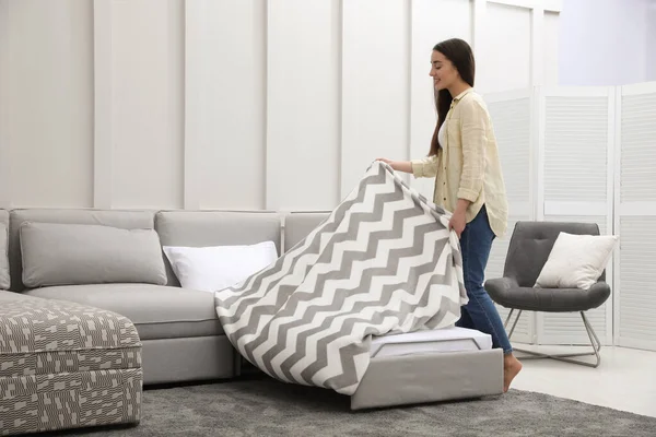 Woman making sleeping place for guest in living room. Convertible sofa