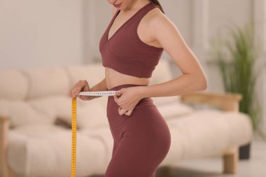 Spor kıyafetli bir kadın, evde bantla ölçü alıyor, yakın plan.