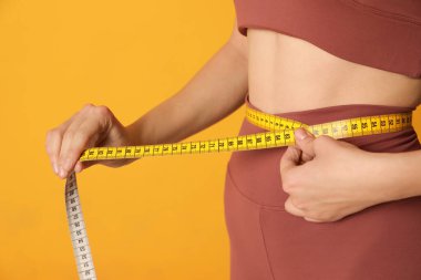 Spor kıyafetli kadın, sarı arka planda bantlı bel ölçüsü, yakın plan.