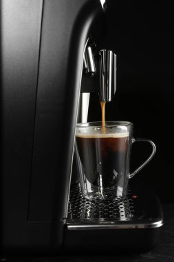 Kahveyi modern espresso makinesiyle gri masada siyah arka planda yapmak.