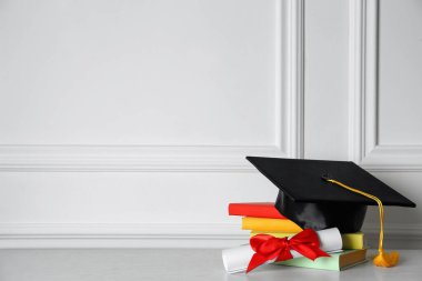 Mezuniyet şapkası, kitaplar ve diploma beyaz duvarın yanında, metin için yer var.