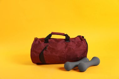 Sarı arka planda spor çantası ve dambıllar.