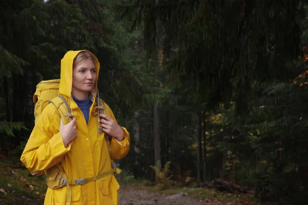 雨の下で森の中でレインコートとバックパックを持つ若い女性 — ストック写真