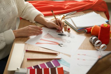 Moda tasarımcısı ahşap masadaki eskiz defterinde yeni kıyafetler yaratıyor.