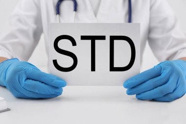 Beyaz masada kısaltması STD olan kağıt tutucu doktor, yakın plan.