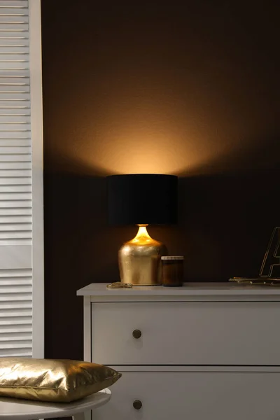 室内の茶色の壁の近くの引き出しの白い胸にスタイリッシュなランプと装飾 インテリアデザイン — ストック写真