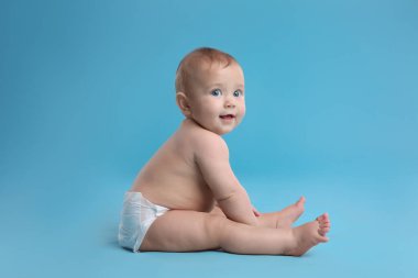 Kuru, yumuşak bezli, açık mavi arka planda oturan şirin bir bebek.