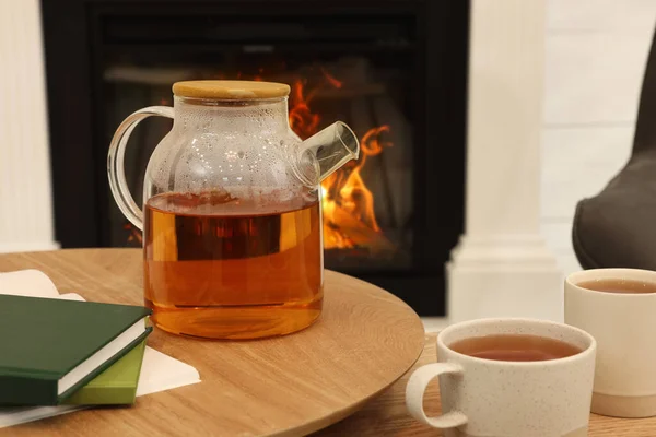 部屋の装飾暖炉の近くの木製のテーブルの上に熱い飲み物や本のカップでティーポット インテリアデザイン — ストック写真