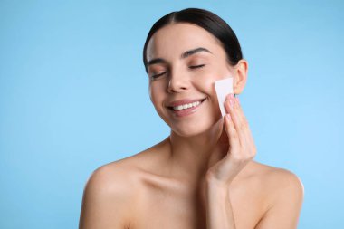 Açık mavi arkaplanda matlaştırıcı mendil kullanan güzel bir kadın