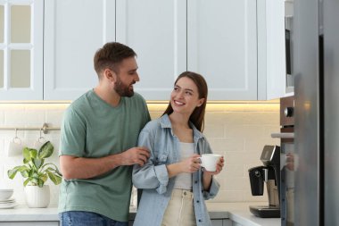 Mutlu çift mutfakta modern makineyle taze aromatik kahve hazırlıyor.