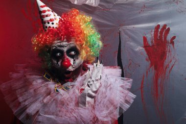 Kan lekeli plastik filmin yanındaki korkunç palyaço. Cadılar Bayramı partisi kostümü