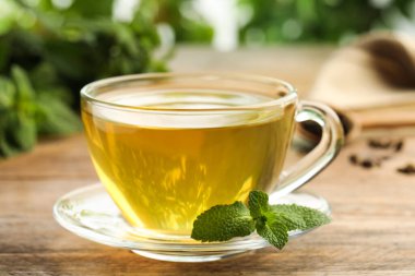 Cam bardakta aromatik yeşil çay, ahşap masada taze nane ile bulanık arka plan, yakın plan
