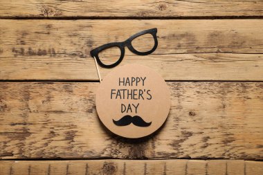 Card with phrase Happy Father's Day and paper glasses on wooden background, flat lay