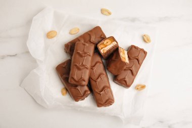 Chocolate bars with caramel, nuts and nougat on white marble table, flat lay