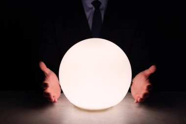 İşadamı, karanlıkta geleceği tahmin etmek için parlak kristal küre kullanıyor. Falcı.