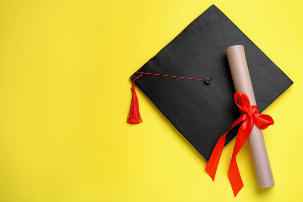 Graduation hat and diploma on yellow background, flat lay. Space for text