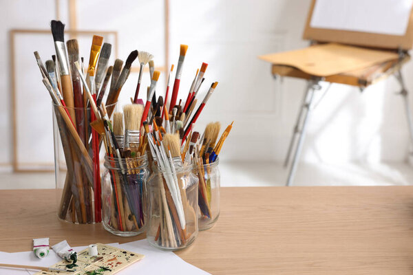 Different brushes, paints and palette on wooden table indoors, space for text. Artist's workplace