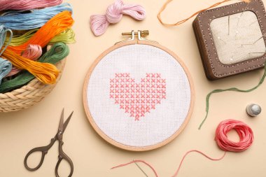 Flat lay composition with embroidery and different sewing accessories on beige background