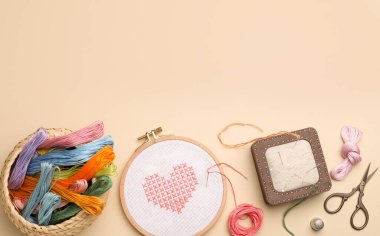 Flat lay composition with embroidery and different sewing accessories on beige background. Space for text