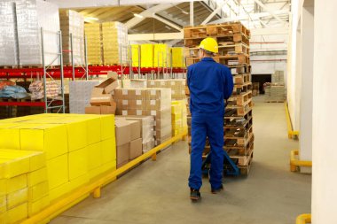 Depoda manuel forkliftle ahşap paletler taşıyan bir işçi.