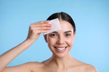 Açık mavi arkaplanda matlaştırıcı mendil kullanan güzel bir kadın