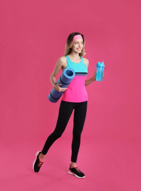 Yoga minderi ve pembe arka planda titreyen güzel bir kadın.