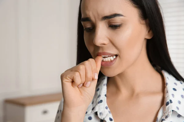 Young woman biting her nails at home