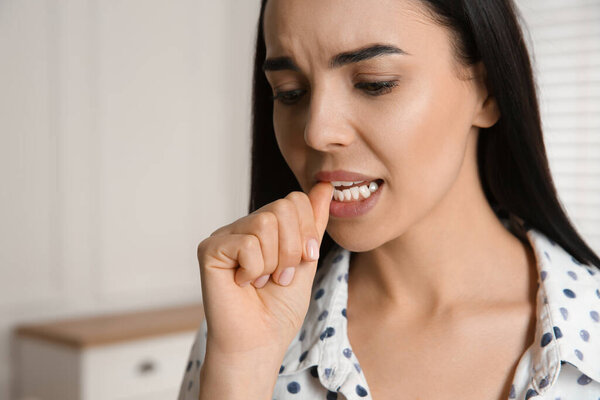 Young woman biting her nails at home