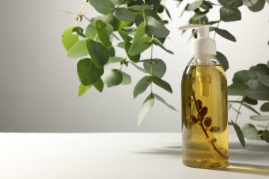 Bottle of liquid soap on white table near eucalyptus branches, space for text