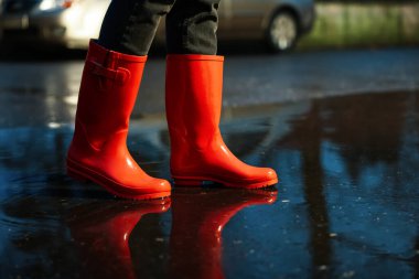 Woman with red rubber boots walking in puddle, closeup. Rainy weather