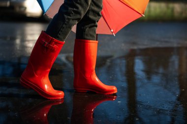 Woman with umbrella and red rubber boots walking in puddle, closeup. Rainy weather