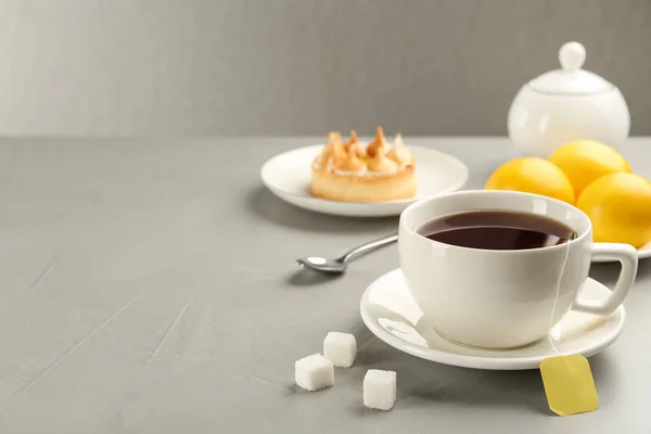 Tea bag in ceramic cup of hot water and sugar on grey table. Space for text