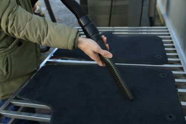 Otomobil halılarını elektrikli süpürgeyle temizleyen adam oto yıkamada, yakın plan.