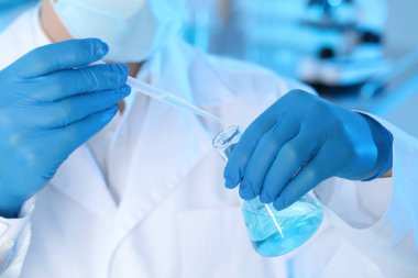 Scientist dripping sample into flask in laboratory, closeup. Medical research