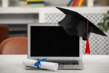 Mezuniyet şapkası, öğrenci diploması ve laptopu beyaz masa içinde.