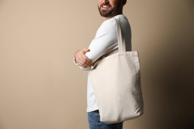 Happy young man with eco bag on beige background, closeup
