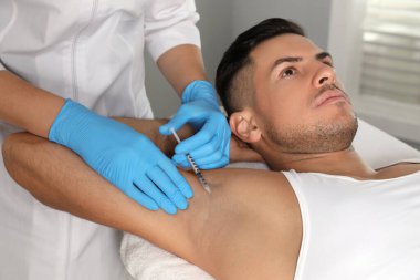 Kozmetik uzmanı klinikte adamın koltuk altına iğne yapıyor. Hiperhidroz tedavisi