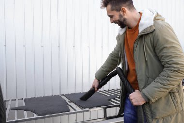 Otomobil yıkama servisinde adam elektrikli süpürgeyle halı temizliyor.