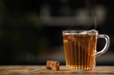 Tea bag in glass cup of hot water and sugar on wooden table against blurred background