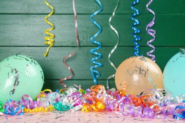 Colorful serpentine streamers, balloons and confetti on pink wooden table